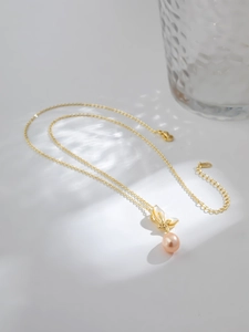 Vue détaillée du pendentif nœud doré avec perle rose et chaîne en or sur fond gris