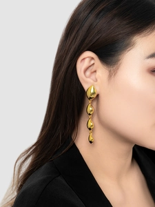 Close-up of cascading gold teardrop earrings with mirror finish on a model