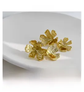 Dettaglio di orecchini a fiore placcati oro 18K con trama vintage su piatto bianco