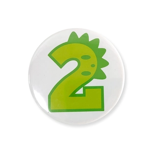 Close-up of a white tinplate badge featuring a green cartoon dinosaur number 2 design