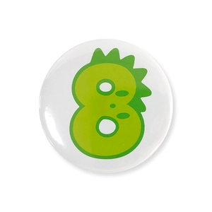 Detail of round tinplate badge featuring a green cartoon dinosaur number 8 on white surface