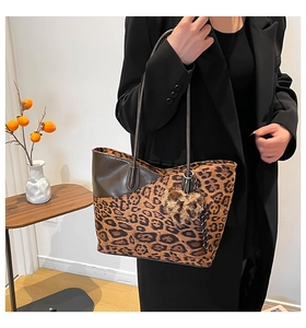 Detail of leopard print tote bag with brown leather trim and plush heart charm accessory