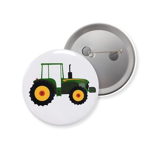 Front and back detail of a round tractor badge with green tractor print and safety pin