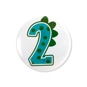 Detail of round tinplate dinosaur badge with teal number two and green fins for kid's birthday