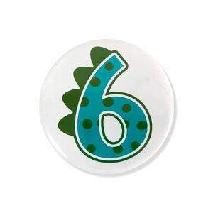 Close-up of a round cartoon dinosaur number 6 badge for kids' birthday party decor
