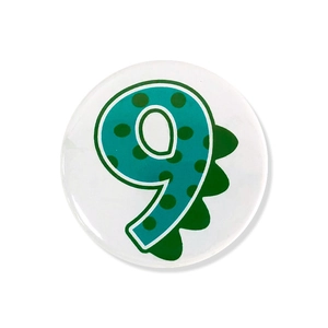 Detailed view of round number 9 dinosaur badge with green polka dots for birthday parties