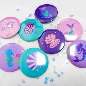 Flat lay view of 8 assorted mermaid themed badges with colorful ocean animal illustrations
