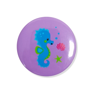 Detail of round purple mermaid badge featuring seahorse, shell and starfish designs