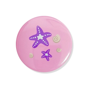 Close-up of a round pink mermaid party badge featuring purple starfish and shell patterns