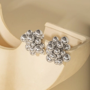 Detail shot of cluster silver metallic ball earrings on a minimalist cream display stand