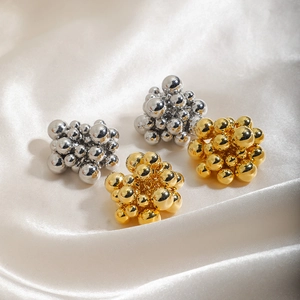 Polished gold and silver metal ball cluster stud earrings on silk fabric background