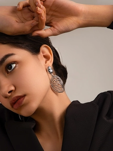 Close-up of large silver hollow wavy earrings with liquid metal texture on a model