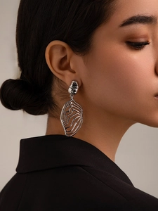 Macro shot of silver metallic leaf statement earrings featuring wavy hollow cutout design