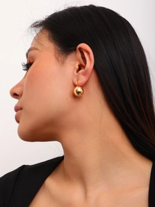 Detail of matte brushed gold spherical earrings worn by a model on a grey background