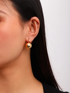 Close-up of 18K gold-plated matte brushed metal ball earring on model earlobe