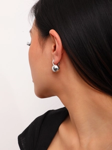 Close-up of a matte brushed silver metal ball earring worn by a model on a neutral background