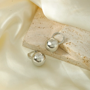 Detailed view of matte brushed metal ball earrings on beige stone and silk background