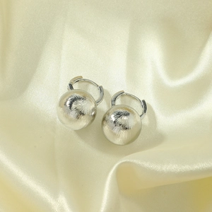 Macro shot of silver sphere earrings featuring a brushed metallic texture on satin
