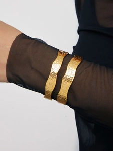 Detail showing wide 18K gold-plated cuffs with hammered texture and wavy edges on model