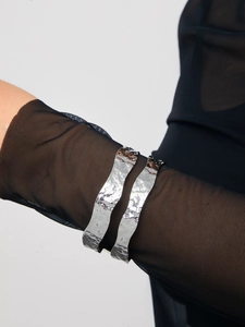 Close-up of hammered silver cuff bracelet worn over black mesh sleeve in modern style