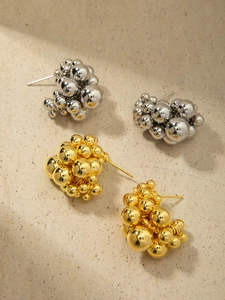 Detail of 18K gold and silver metal ball cluster earrings on stone background