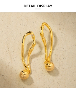 Gros plan détaillé des boucles d'oreilles courbées en or 18K avec sphère métallique polie