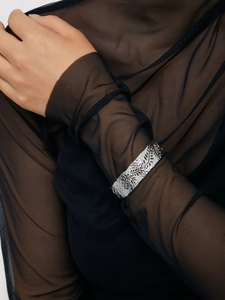 Close-up of a silver-toned open leaf bracelet with intricate floral etching on a wrist