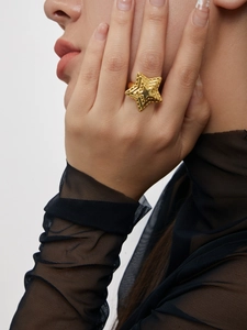 Détail d'une bague étoile dorée à texture relief portée sur le doigt d'un mannequin