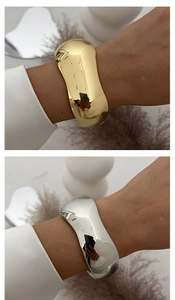 Macro view of wide irregular wave cuff bracelets in mirror polished gold and silver