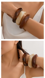 Macro detail of three wide acrylic resin bangles in amber and creamy white tones
