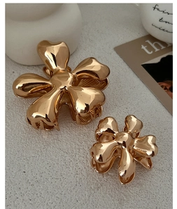 Detail of high-shine gold flower hair claws in large and small sizes on white surface