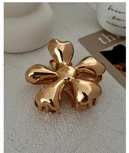 Detail of a shiny gold five-petal flower hair claw clip with a polished metallic finish