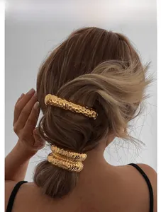 Détail d'une pince à cheveux et d'élastiques en métal doré martelé sur cheveux