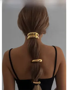 Detail shot of four polished gold metal ring hair ties on a sleek low ponytail