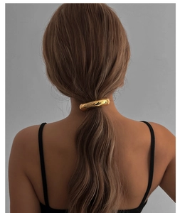 Attache-queue de cheval dorée au design incurvé minimaliste sur les cheveux d'un modèle