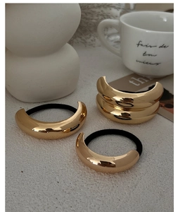 Detailed view of three golden crescent hair ties with black elastic bands on a white surface