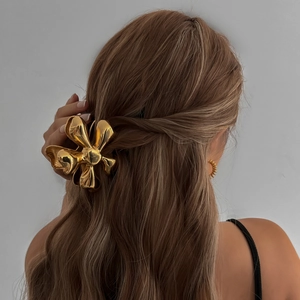Elegant gold flower hair claw clip displayed on a woman's brown hair from the back