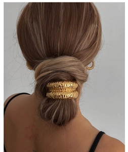Detailed view of a gold metallic hair ring featuring a textured hammered finish on a bun