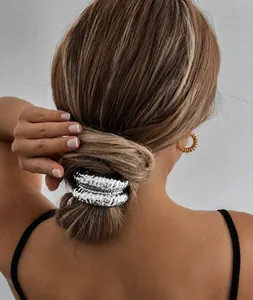 Close-up of a silver crinkled metal hair tie worn on a sleek low bun hairstyle