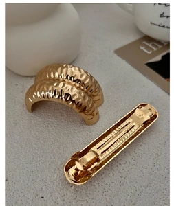 Detail of a wavy gold metal hair clip with a textured surface and spring mechanism