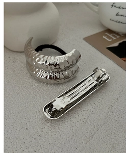 Detail of silver hammered metal hairband and floral engraved clip on textured background