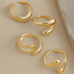 Detail view of four irregular lava style gold rings with mirror finish on beige surface