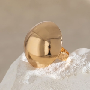 Macro detail of polished gold-tone chunky dome ring on a textured white stone base
