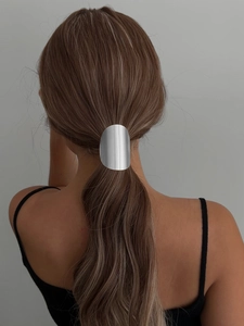 Detail of a minimalist silver oval metal hair cuff securing a low ponytail on a model