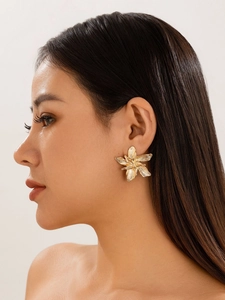 Nahaufnahme eines großen goldenen Blumen-Ohrsteckers mit texturierten Blüten auf einem Model