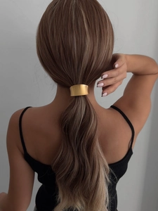 Close-up of a matte gold curved metal hair cuff on a low ponytail hair style