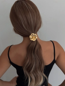 Detailed view of a metallic golden flower hair accessory on a model's ponytail