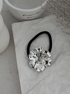 Detailed macro of a large silver alloy flower hair tie with textured petals and elastic band