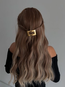 Détail d'une pince à cheveux rectangulaire dorée ajourée sur de longs cheveux bruns