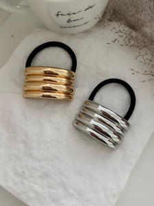 Dettaglio di elastici per capelli metallici oro e argento con texture ondulata su bianco